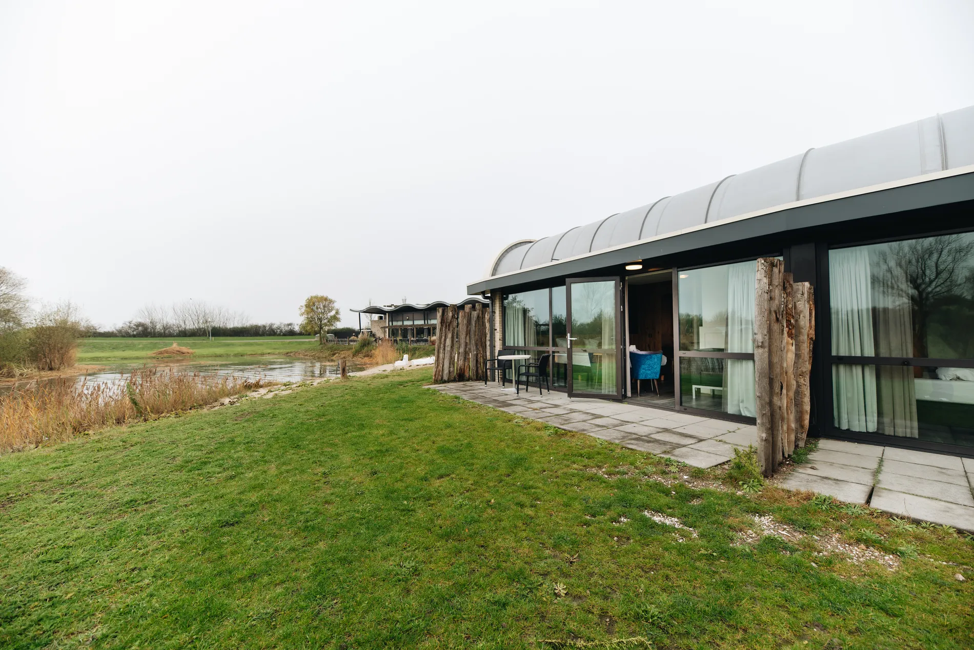 Exterieur van de unieke geschakelde lodges bij Resort Land & Zee, gelegen aan een vijver met een ruim grasveld en eigen terras.